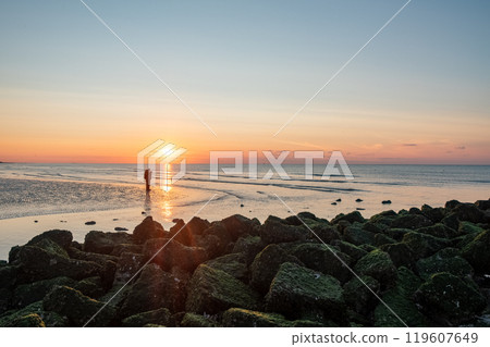 A Beautiful Scenic Sunset Over a Tranquil Beach Complemented by a Rocky Shoreline View 119607649