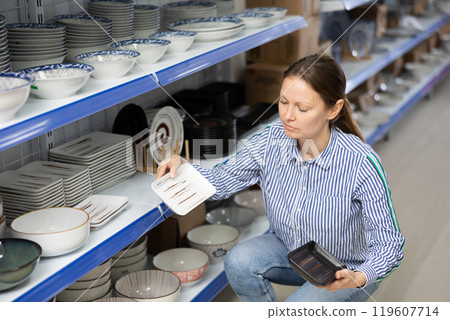 Woman in supermarket is choosing square plates Woman in supermarket is choosing square plates 119607714