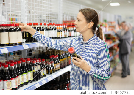 Woman customer is thinking about buying spicy and unusual soy sauce. Woman customer is thinking about buying spicy and unusual soy sauce. 119607753