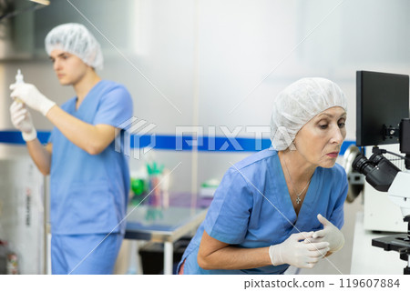 Female veterinary microscopist examining blood samples of animal patient in laboratory 119607884