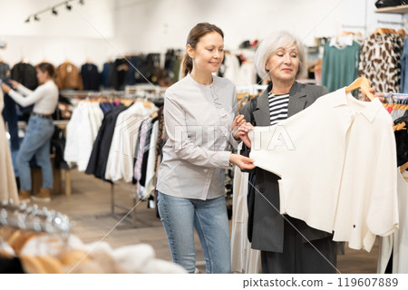 Two satisfied female customers choosing cardigan or jacket in clothing boutique 119607889