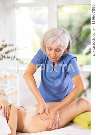 Elderly woman giving thigh massage to young woman 119607890