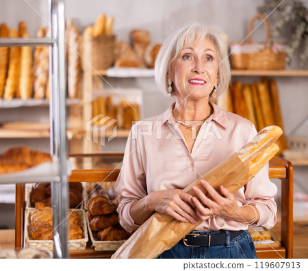 Mature female shopper with paper bag of fresh hot bread and baguettes in bakery Mature female shopper with paper bag of fresh hot bread and baguettes in bakery 119607913