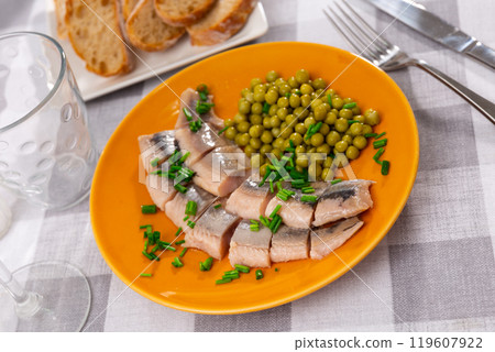 Appetizing saltes slices herring fillet with canned green peas served on plate 119607922