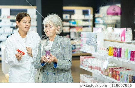 Girl pharmacist helps senior woman buyer to decide on choice of lubricant. Girl pharmacist helps senior woman buyer to decide on choice of lubricant. 119607996