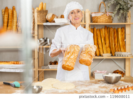 Senior female baker worker show loafs of breads 119608011