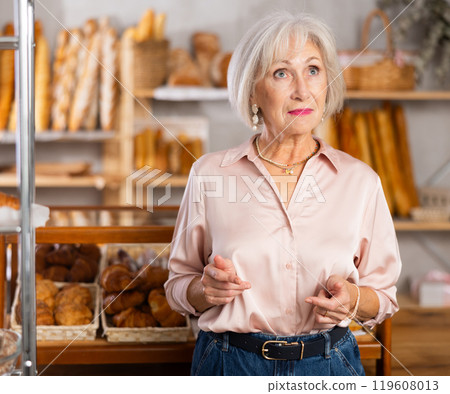 Mature European woman near window of bakery food court store examines assortment Mature European woman near window of bakery food court store examines assortment 119608013