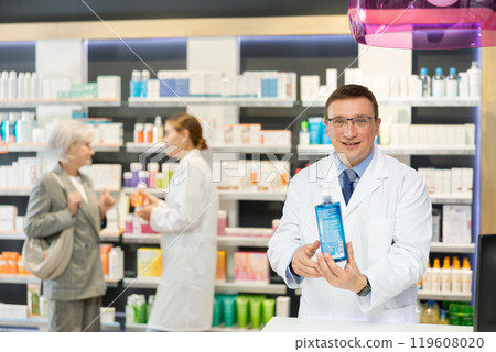 In pharmacy, male specialist holds and shows new effective remedy for moisturizing delicate skin 119608020