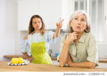 Quarrel of an elderly mother and adult daughter in the kitchen. Adult daughter is unhappy with elderly mother Quarrel of an elderly mother and adult daughter in the kitchen. Adult daughter is unhappy with elderly mother 119608110