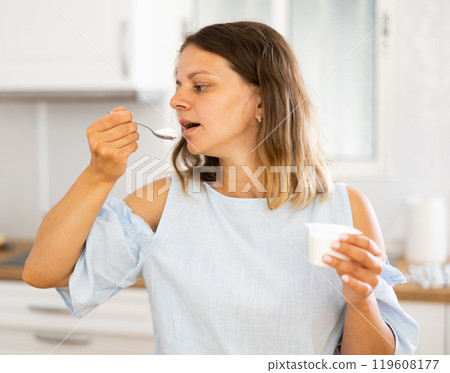 Young woman eating tasty yogurt in kitchen 119608177
