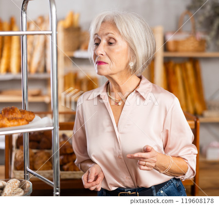 Mature European woman near window of bakery food court store examines assortment Mature European woman near window of bakery food court store examines assortment 119608178