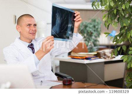 Male doctor examining x-ray closely in clinic 119608329