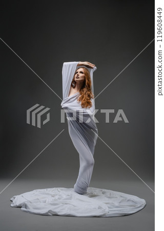 A dancer in a flowing white fabric striking an elegant pose in a studio 119608449