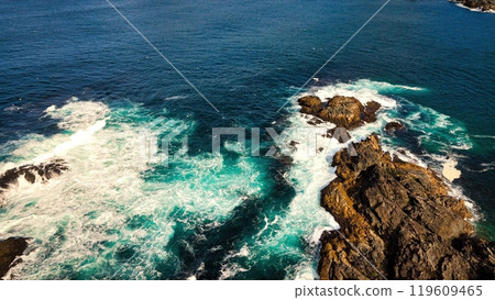 Stunning Aerial View of Vibrant Turquoise Waves Elegantly Crashing Against Rocky Shoreline 119609465