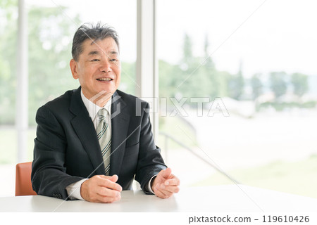 一位身著西裝的亞洲資深男性商人坐在辦公桌前 一位身著西裝的亞洲資深男性商人坐在辦公桌前 119610426