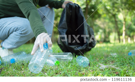 Woman of dedicated volunteers are participating in an environmental cleaning activity in a park. Woman wearing gloves and hold large black bags. Woman collecting trash and plastic bottles in a park. 119611136