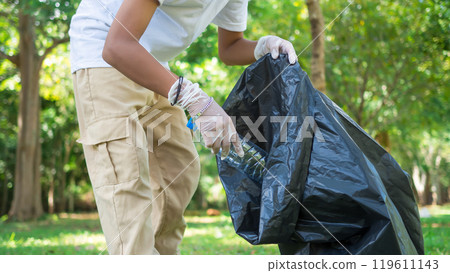 A boy of dedicated volunteers are participating in an environmental cleaning activity in a park. Boy wearing gloves and hold large black bags. Boy collecting trash and plastic bottles in a park. A boy of dedicated volunteers are participating in an environmental cleaning activity in a park. Boy wearing gloves and hold large black bags. Boy collecting trash and plastic bottles in a park. 119611143