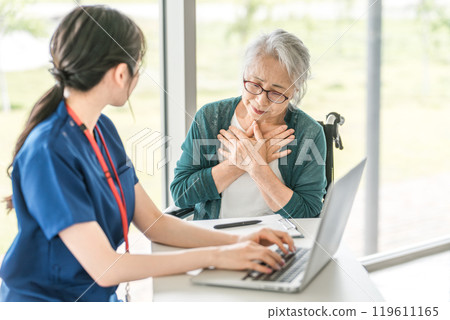 Senior woman and female nurse informing doctor of illness at hospital/care facility (medical examination/health checkup) 119611165