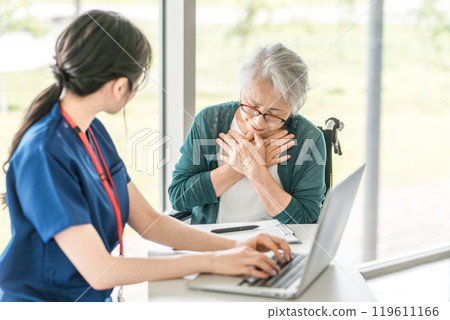 Senior woman and female nurse informing doctor of illness at hospital/care facility (medical examination/health checkup) 119611166