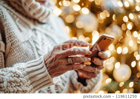Elderly woman using smartphone with festive lights in the background. Concept of traditional greetings for New Year and Christmas 119611250