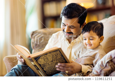 Indian family, father and son reading a book together in a cozy living room 119611251