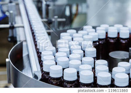 Glass bottle with cap on production line of conveyor belt at filling machine in medical factory. pharmaceutical and supplement manufacturing. Glass bottle with cap on production line of conveyor belt at filling machine in medical factory. pharmaceutical and supplement manufacturing. 119611860