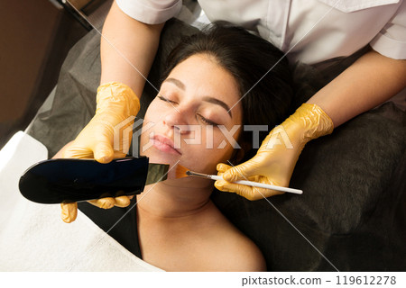Cosmetologist performing ultrasonic facial cleansing with scrubber and brush 119612278