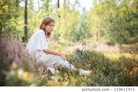 A young child sitting quietly in a serene forest, surrounded by vibrant greenery 119612453