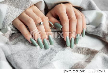 Elegant mint green manicure on long nails adorned with a ring, wrapped in a cozy blanket  119612511