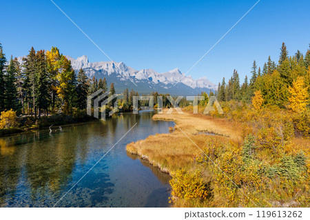 A river through a field of grass with mountains in background in autumn. Spring Creek Boardwalk, Policeman Creek Trail. Canmore, Alberta, Canada. 119613262