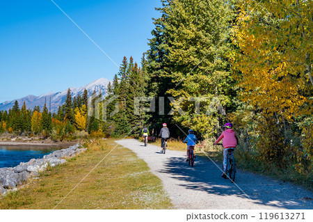 People cycling along the Bow River walking trail in autumn. Canmore, Alberta, Canada. Higashikawa Friendship Trail. 119613271