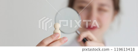 Woman looks at wooden figurine in hand through loupe 119613418