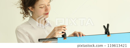Woman attaches blue paper background to tripod stand Woman attaches blue paper background to tripod stand 119613421
