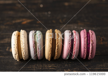 Macaron set of different flavors and colors with almond flour on a dark wood background. Macaroon cookies in low key 119615000