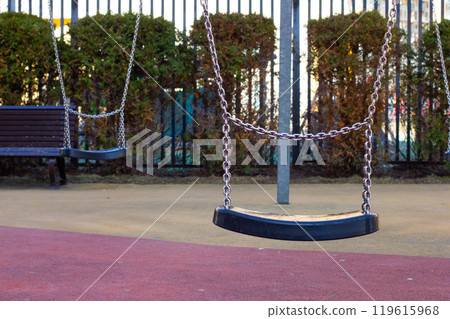 Empty swings on a playground evoke sadness and loneliness, metal chains gently swaying in the wind. Empty playground with swings. Lonely swings on a playground. Empty swings on a playground evoke sadness and loneliness, metal chains gently swaying in the wind. Empty playground with swings. Lonely swings on a playground. 119615968