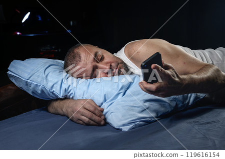 Man with smartphone in bed at night. Handsome man using mobile phone in bed.. Man with smartphone in bed at night. Handsome man using mobile phone in bed.. 119616154