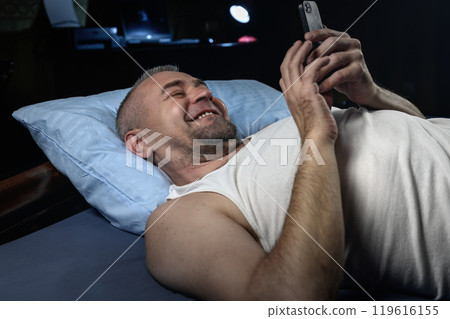 Man with smartphone in bed at night. Handsome man using mobile phone in bed.. Man with smartphone in bed at night. Handsome man using mobile phone in bed.. 119616155