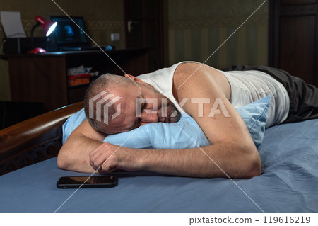 Man with smartphone in bed at night. Man sleeping in bed next to mobile phone. Man with smartphone in bed at night. Man sleeping in bed next to mobile phone. 119616219