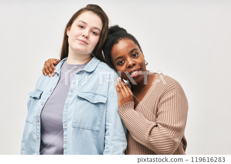 Two friends standing together while embracing each other wearing casual attire and smiling. Background is plain and minimal, focusing on the genuine moment shared between them 119616283