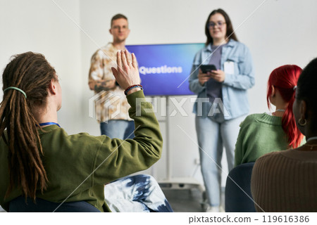 People participating in an interactive discussion during a questions and answers session with one individual raising hand asking a question 119616386
