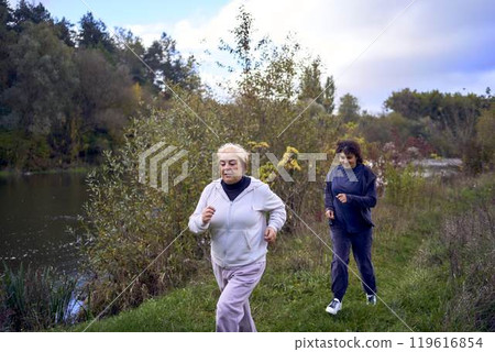 A middle-aged woman and her old mother take a morning jog together to maintain health by the river in autumn A middle-aged woman and her old mother take a morning jog together to maintain health by the river in autumn 119616854
