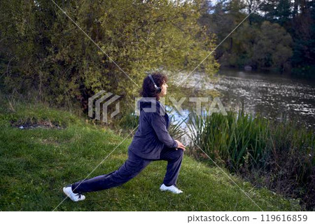 middle-aged woman exercising and switching music in her wireless headphones using her phone during a morning jog in an autumn park 119616859