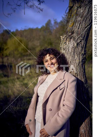 middle-aged woman with dark curly hair in light beige suit and coat enjoying nature in autumn forest middle-aged woman with dark curly hair in light beige suit and coat enjoying nature in autumn forest 119616875