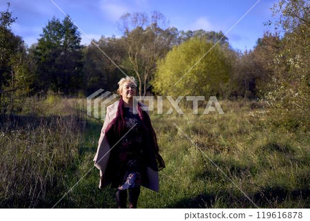 elderly woman with gray hair in light beige coat enjoying nature in autumn forest 119616878