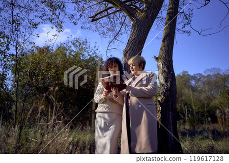 middle-aged woman and elderly mother with holy bible in hands praying for peace in autumn forest 119617128