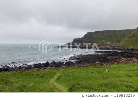 Tourists explore rocky cliffs and shoreline of Giant's Causeway as Atlantic stretches under grey sky Tourists explore rocky cliffs and shoreline of Giant's Causeway as Atlantic stretches under grey sky 119618239