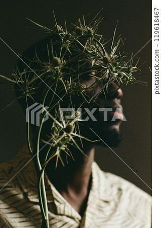 Artistic close up portrait of young African American man with eryngium plant hiding face shot on film with grain 119618467