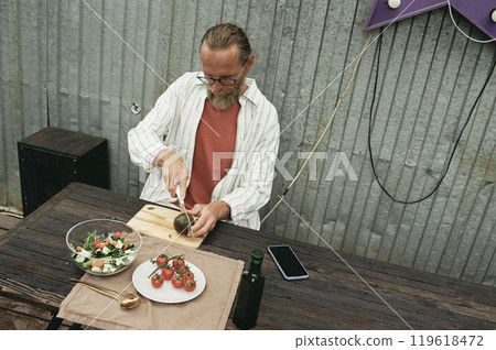 Minimal retro film shot of modern senior man cooking outdoors and cutting vegetables for salad copy space 119618472