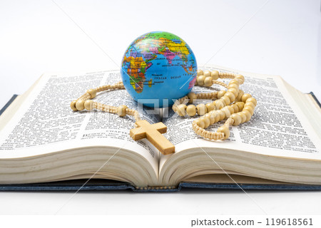 Opened book of Holy Bible with rosary beads and globe. It is laying on white background. Symbol of faith and worship in God 119618561