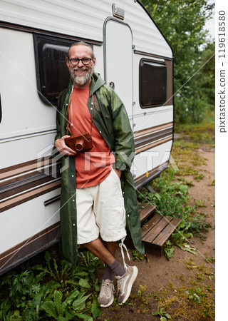 Vertical full length portrait of adult man as tourist travelling by van in nature and smiling at camera Vertical full length portrait of adult man as tourist travelling by van in nature and smiling at camera 119618580
